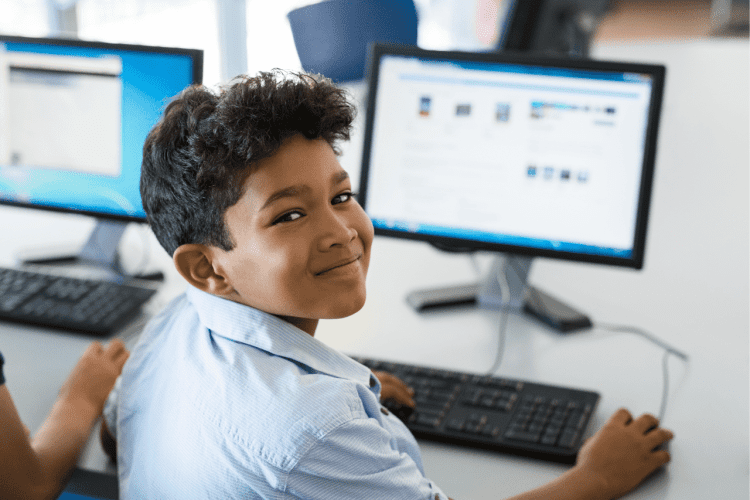 a boy turning his head , behind the computer monitor and keyboard